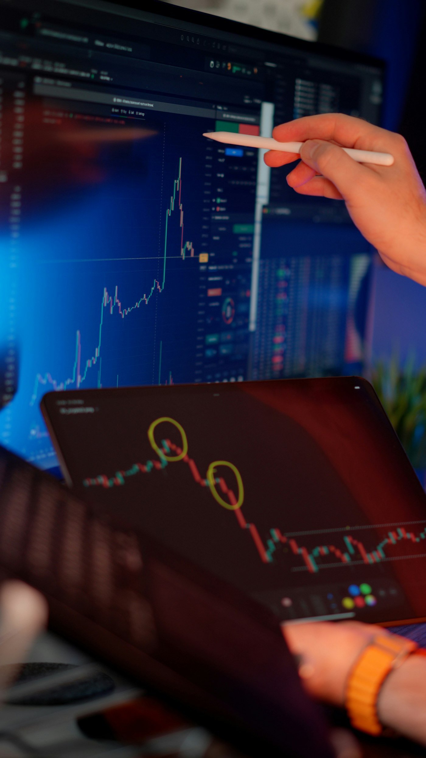An analyst reviewing financial charts on a tablet and screen