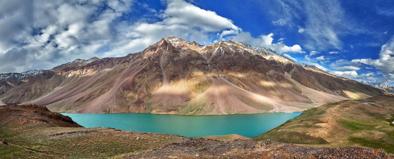 A turquoise lake beneath sunlit mountains under a blue sky